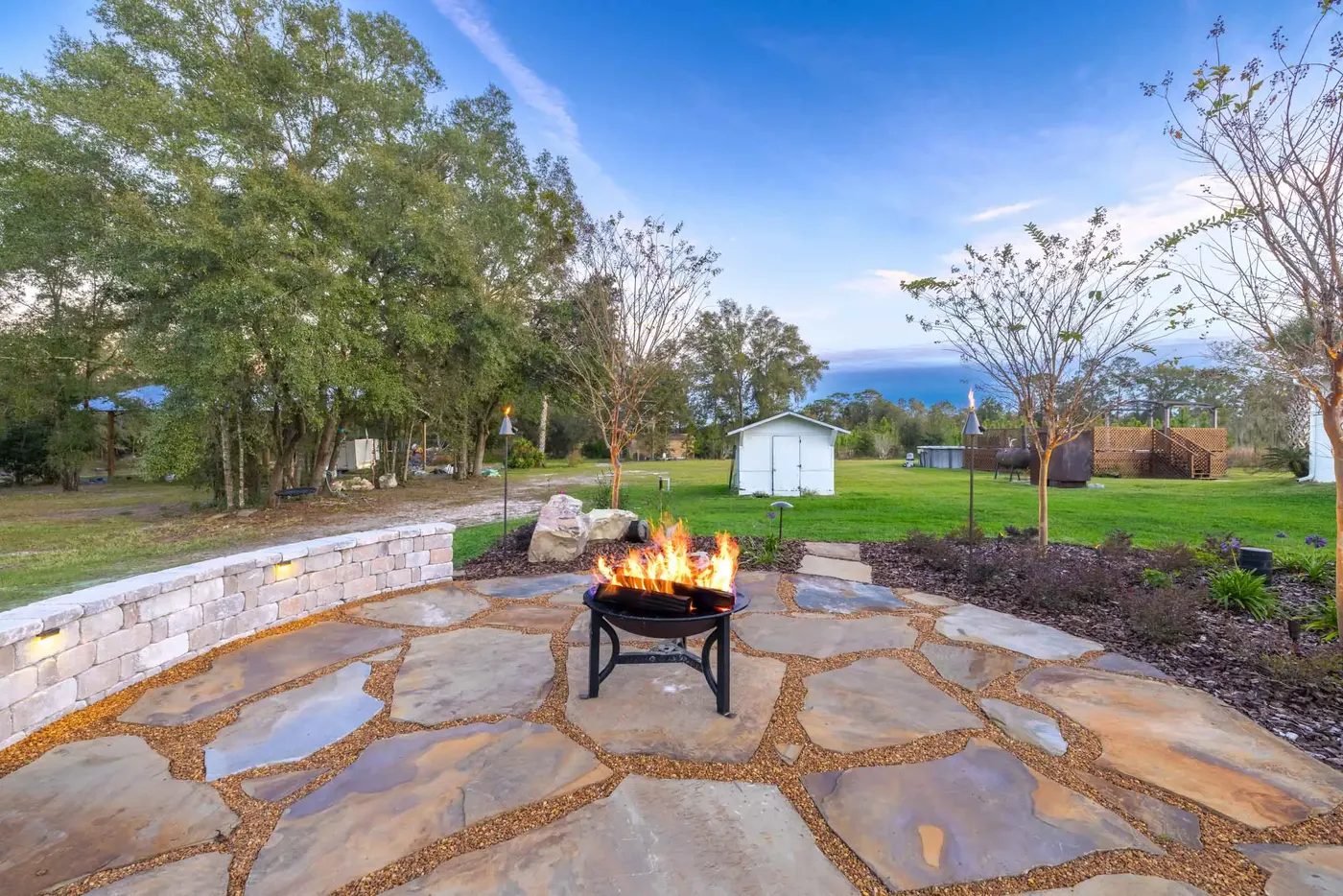 Flagstone patio with a lit fire pit at dusk, seating wall and lawn behind, Gainesville, FL